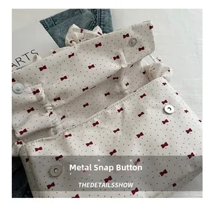 Detail of the metal magnetic buckle on the white pleated bag with red ribbon bow