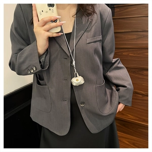 Mini white leather headphone pouch accessory styled as a neck pendant on a grey blazer