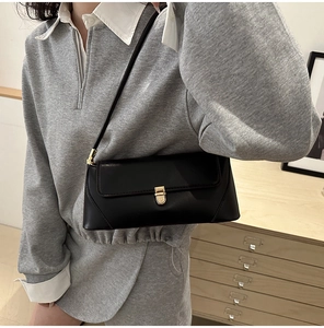 Detail of a black leather baguette bag with golden buckle worn as a shoulder bag