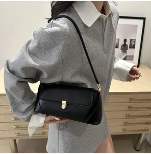Fashionable black leather baguette bag with a golden turn-lock closure on model's shoulder