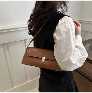 Detail of a brown leather shoulder bag featuring a stylish gold metal clasp closure