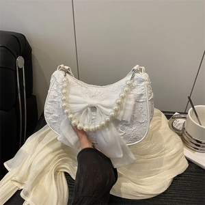 Sac à main blanc texturé avec un grand nœud et une poignée en perles sur une table