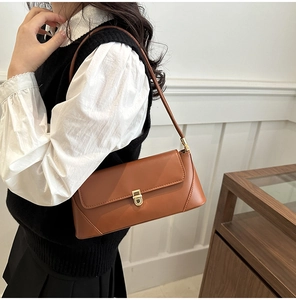 Close-up of caramel leather baguette bag with gold metal buckle on a side-wearing model