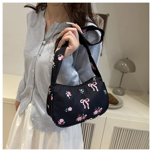 Detail of trendy black crossbody bag with pink rose and bow prints in a lifestyle setting
