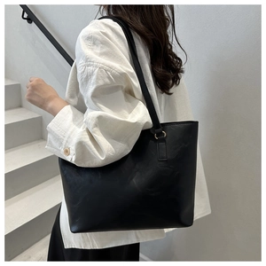 Detailed view of black minimalist tote bag with smooth faux leather on model's shoulder