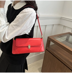 Detail of red leather baguette bag featuring a gold buckle and sleek shoulder strap