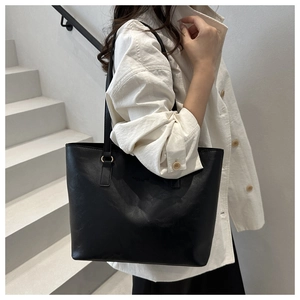 Close-up of minimalist black leather tote bag with gold hardware on white background