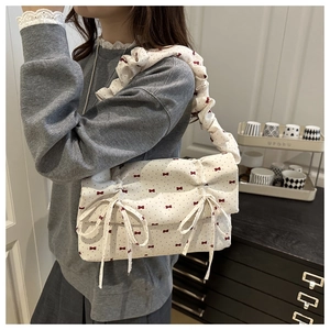 Detail of cream shoulder bag featuring red bow prints and a ruffled cloud-style strap