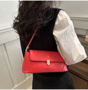 Detail of red leather baguette bag with gold lock worn by a model in a stylish outfit