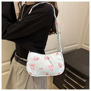 Close-up of a light blue shoulder bag with floral and red bow patterns on a model