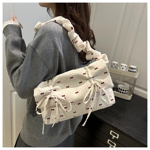 Detail showing cream canvas shoulder bag with red bow pattern and ruffled handle design