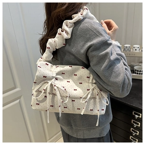 Detail of white pleated handbag with red bow pattern and soft shoulder strap on model