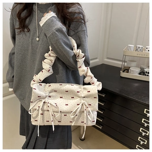 Detailed view of cream fabric shoulder bag with red bow prints and ruffled strap detail