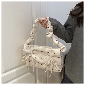 Detail of a cream canvas handbag featuring red polka dots and decorative bows on front