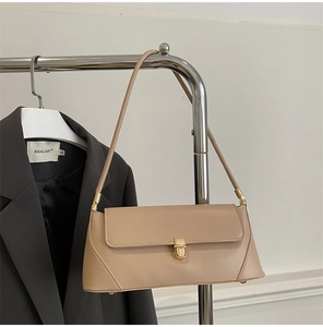 Detail of beige baguette bag with gold metal buckle hanging on a suit hanger