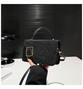Detail of black glitter shoulder bag with golden geometric clasp and leather handle