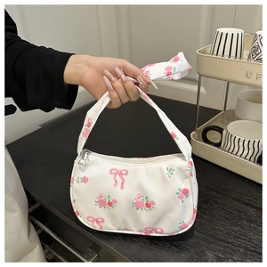 Close-up of white crossbody bag with pink rose and bow prints held by a hand