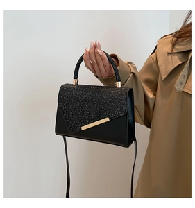 Detail of black crossbody bag with glitter panels and elegant gold metal trim on the flap