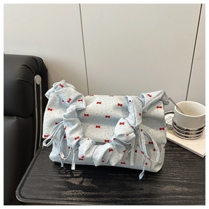 Close-up of light blue pleated handbag featuring red bow patterns and drawstring detail