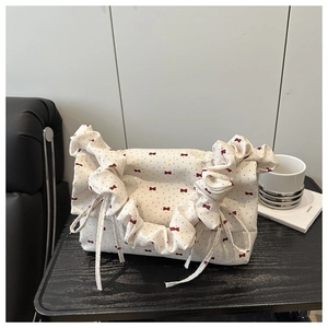Detail of cream pleated handbag with red bow print and ruffled handle on a black table