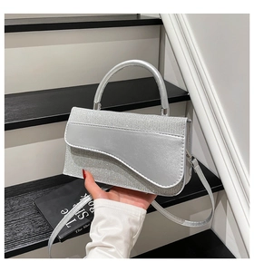 Close-up of glittery silver saddle handbag with curved flap and metallic handle