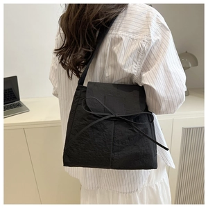 Detailed view of black nylon shoulder bag with crinkled texture and bow detail on a model