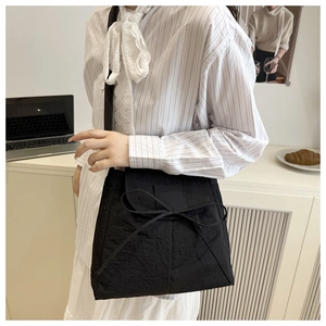 Detail of black nylon shoulder bag with bow tie design and wrinkled texture on model