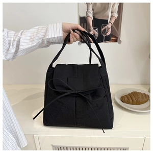 Detail of black nylon tote bag featuring a decorative bow tie and wrinkled texture