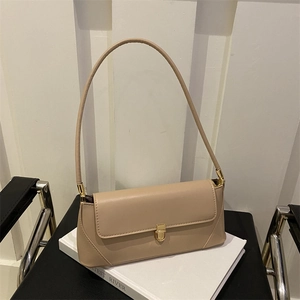 Minimalist beige leather baguette bag with golden buckle on a decorative book stand