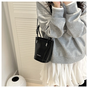 Detail of black glossy bucket bag featuring silver metal handles and fashion logo