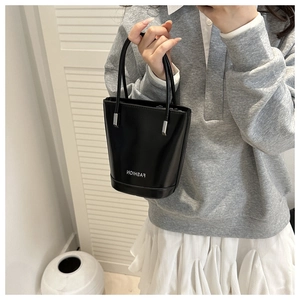 Chic minimalist black faux leather bucket bag shown held by hand in a mirror view