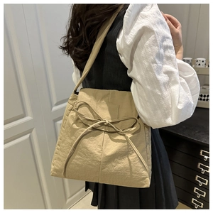 Detail of beige tote bag featuring a decorative ribbon bow and soft textured fabric