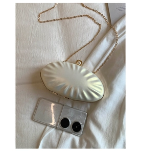 Detail of cream white shell clutch with pearl clasp and golden metal chain link