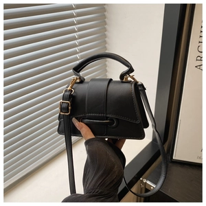 Detail of black trapezoid handbag showing gold buckles and adjustable shoulder strap
