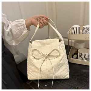 Detail of cream nylon tote bag with large decorative bow on front handle