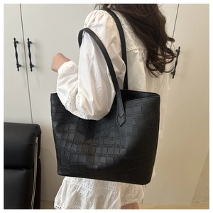 Detail of black faux leather tote bag with crocodile embossing worn on the shoulder
