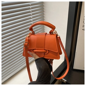Detail of bright orange mini leather handbag with oversized curved handle and gold buckle