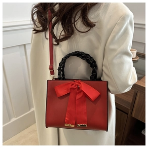 Détail du sac en cuir rouge avec grand nœud en soie et poignée tissée noire sur modèle