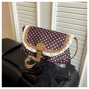 Detail view of lace trim, pink polka dot pattern and leather buckle on crossbody bag
