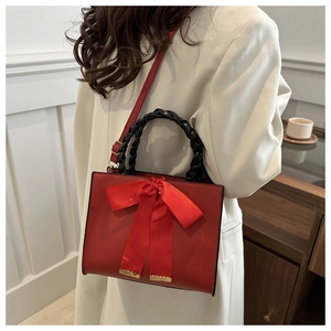 Sac de mariage rouge carré avec nœud décoratif et poignée tressée sur veste beige