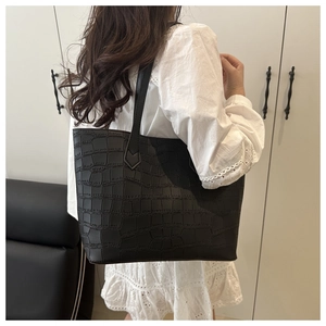 Detail view of large black tote bag with embossed crocodile texture and dual shoulder straps
