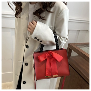 Détail du sac rouge avec un grand nœud en soie et une poignée tissée noire