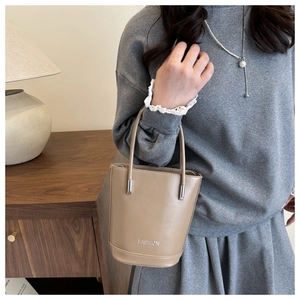 Detail of a beige bucket bag with silver cylinder accents and FASHION logo print