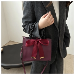 Détail d'un sac à main bordeaux élégant avec un grand nœud en satin et poignée tressée