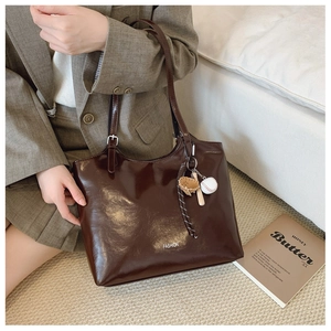 Detail of dark brown glossy tote bag with fashion logo and baseball charm accessory
