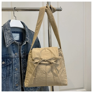 Detail of beige nylon crossbody bag with flap and decorative bow knot on wooden door
