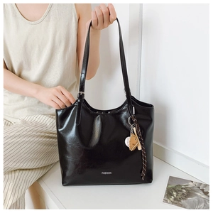 Detail of black glossy leather tote bag with white FASHION text and baseball charm