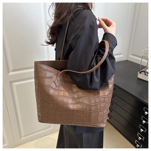 Side view of a large dark brown crocodile pattern tote bag worn on a woman's shoulder