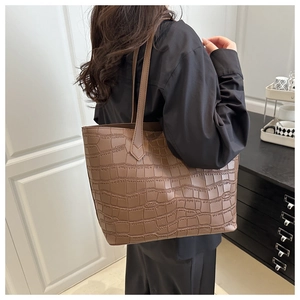 Brown tote bag with crocodile pattern worn by model in a stylish home setting