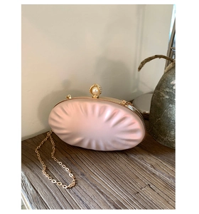 Detail of champagne shell evening clutch featuring pearl clasp and gold chain strap